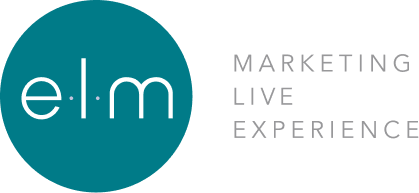 A close-up of an elm tree's textured bark and green leaves against a clear blue sky.